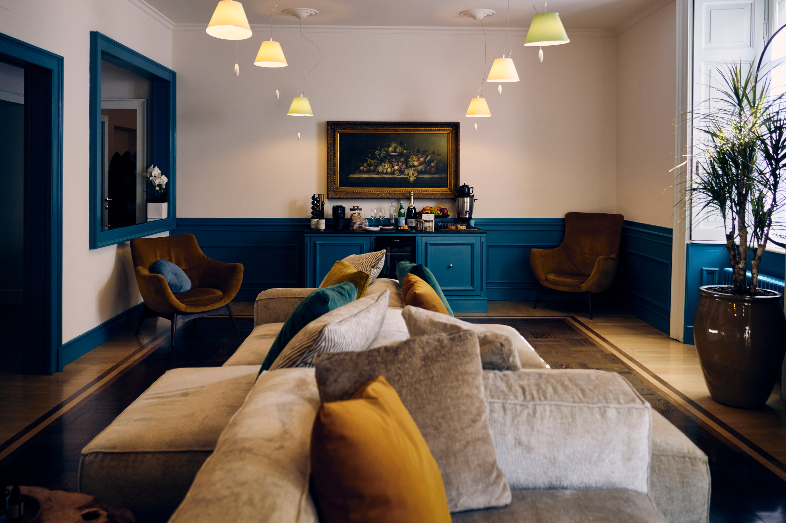 Il salotto di Blum: divano e poltrone davanti alla boiserie blu, con le lampade accese